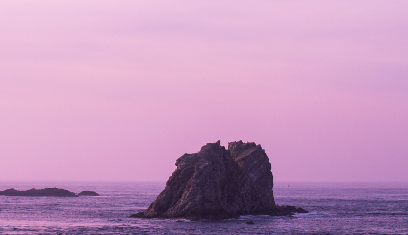 rock in middle of water with a pink sky background